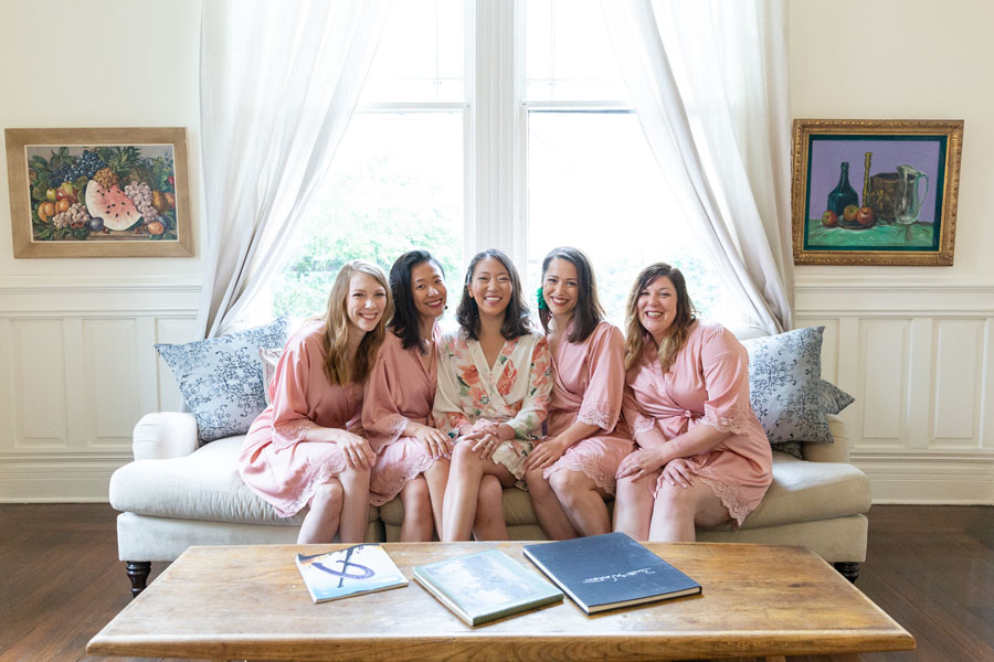 Jenny sits on couch with bridesmaids in pink robes