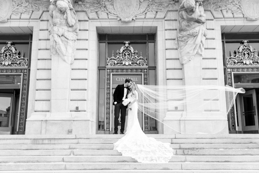 black and white photo of bride and groom kissing outside San Francisco City Hall entrance