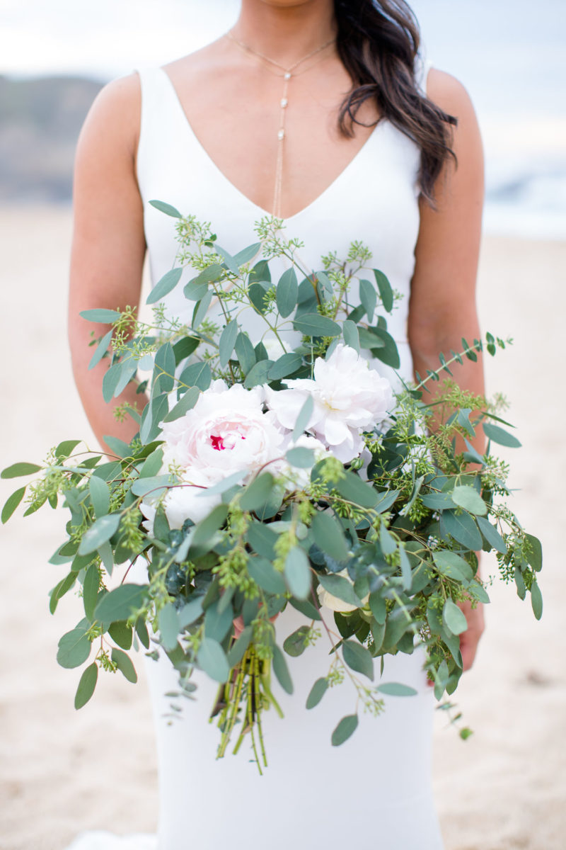 bride holding large bouquet with a lot of greenery on beach